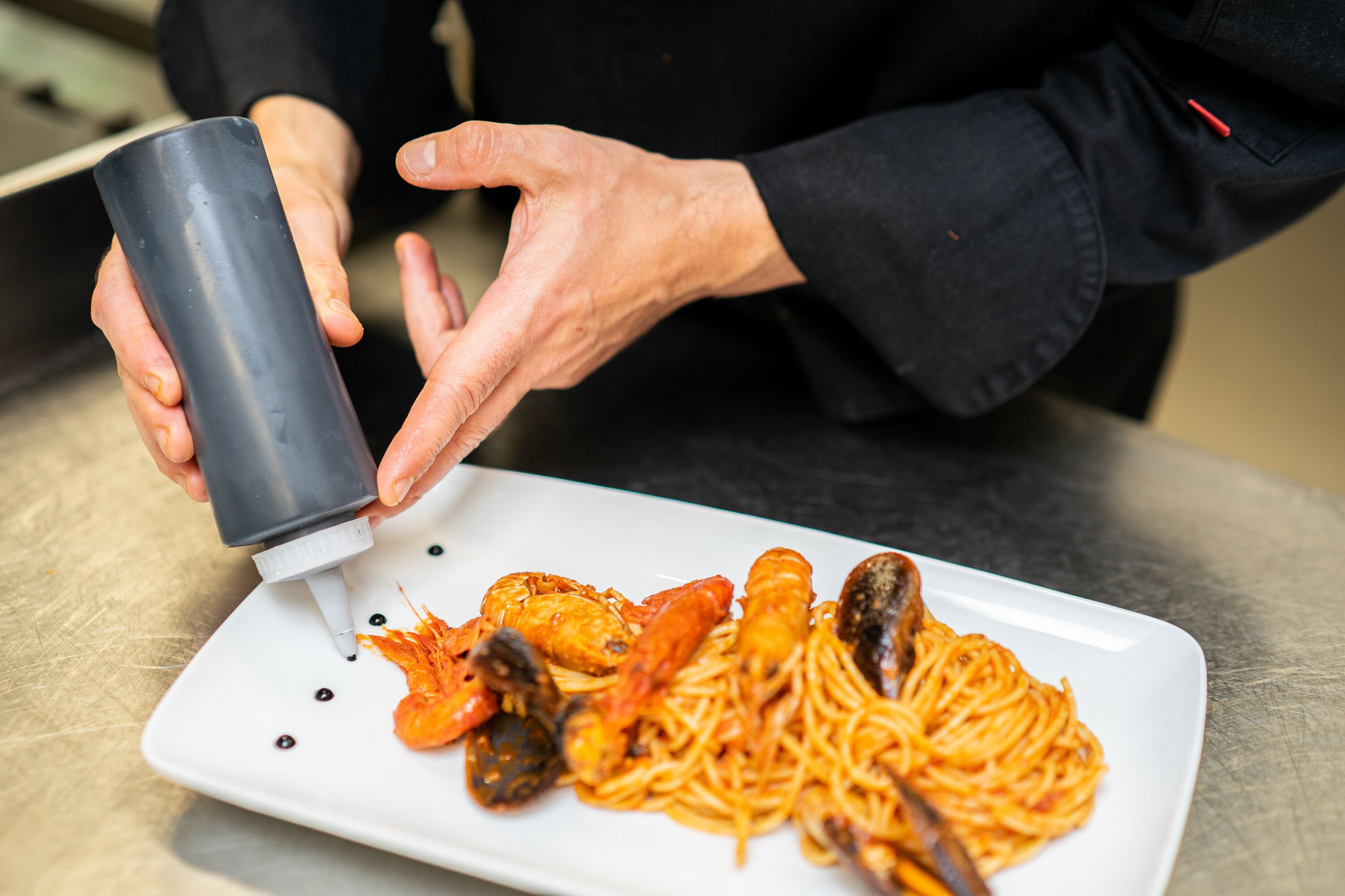 Une personne verse de la sauce sur une assiette de spaghettis aux fruits de mer.