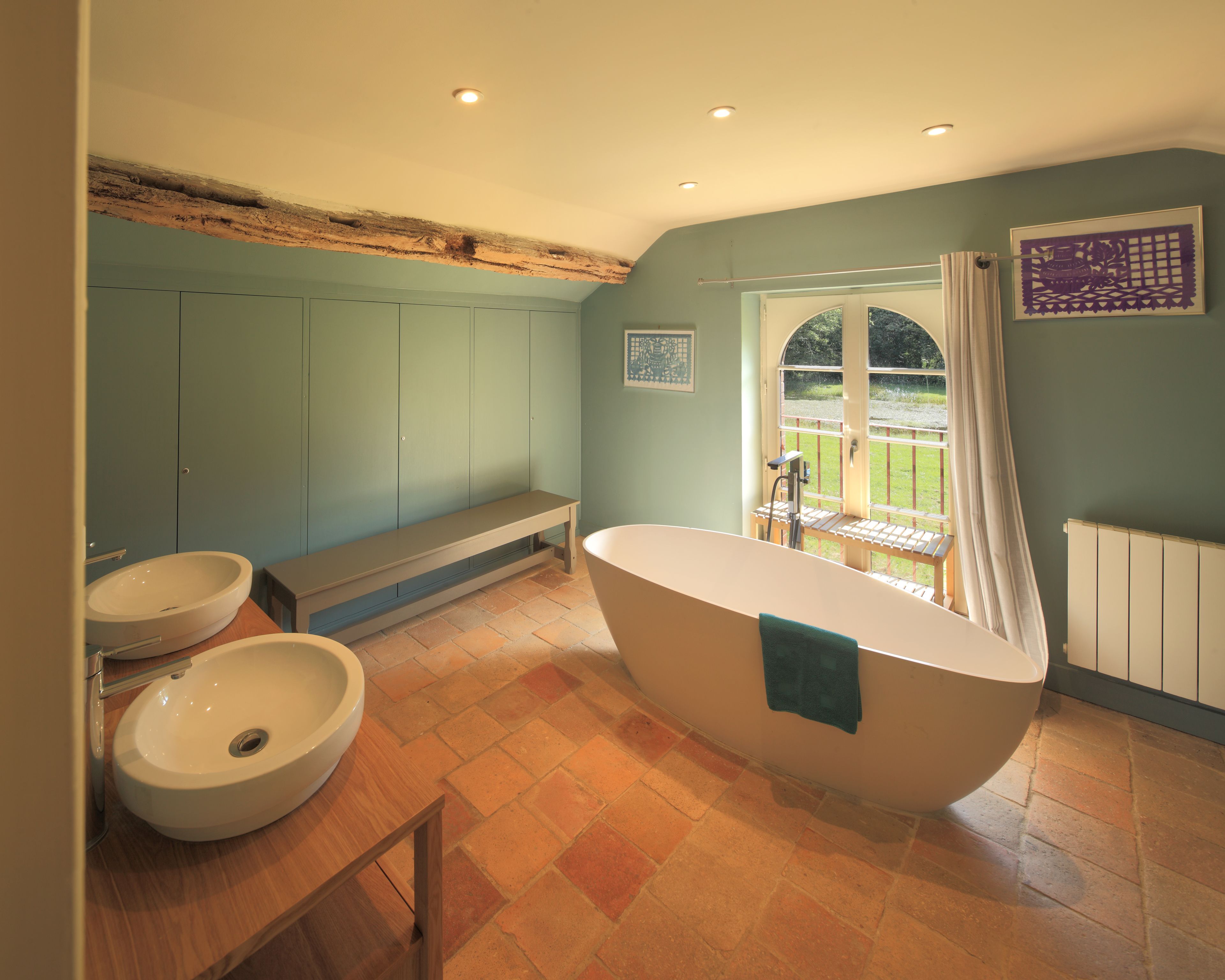 A bathroom with a freestanding bathtub, two sinks, and a bench.