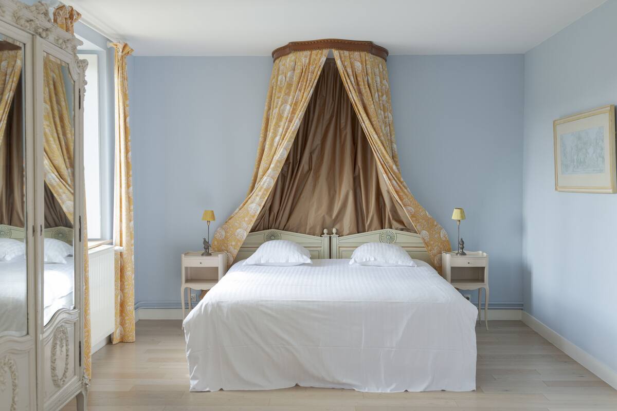 Une chambre à coucher avec un lit à baldaquin, deux tables de chevet avec des lampes, une commode et un tableau encadré au mur.