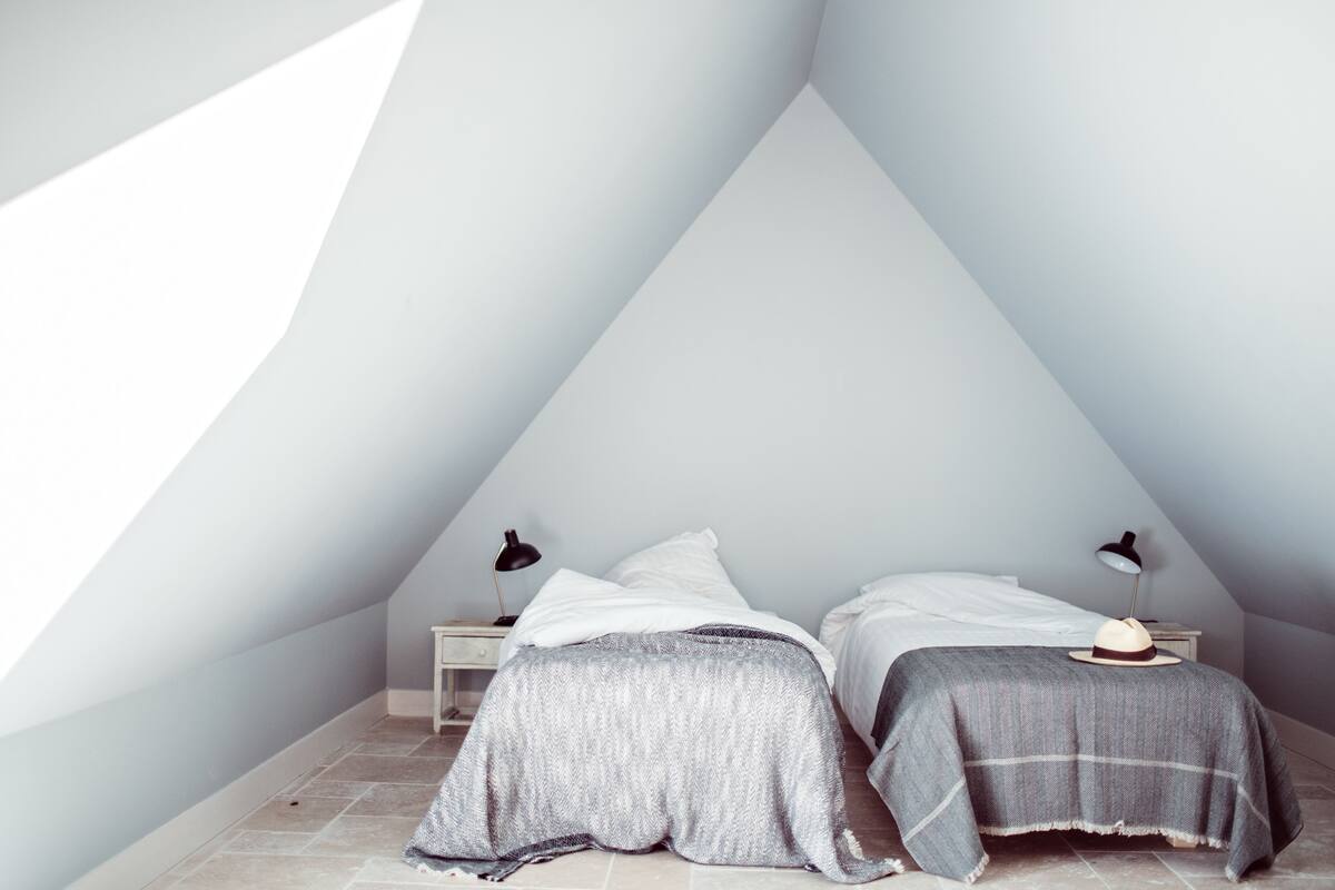 Une chambre avec un plafond en pente, deux lits avec des têtes de lit assorties, des lampes de chevet et une petite table de chevet.