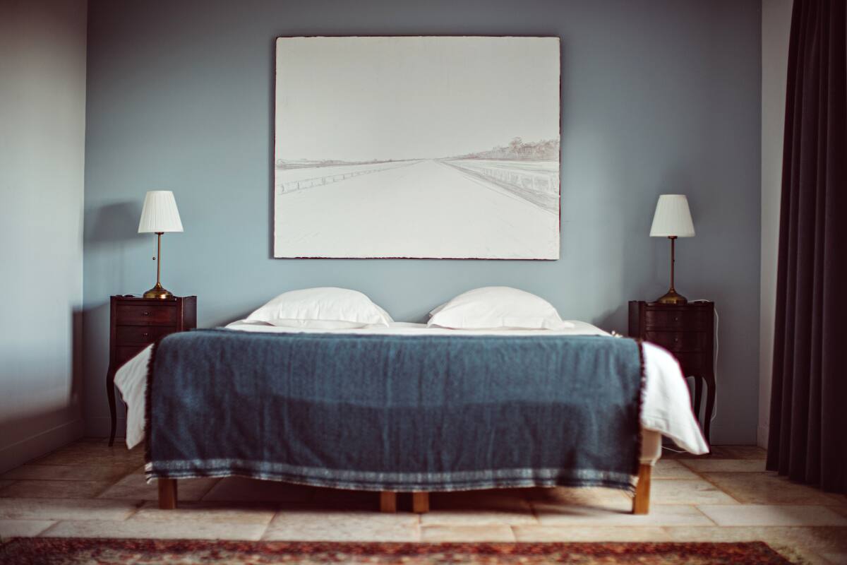 Une chambre à coucher comprenant un lit, deux tables de chevet, une commode, un grand tableau encadré au mur et un tapis à motifs.
