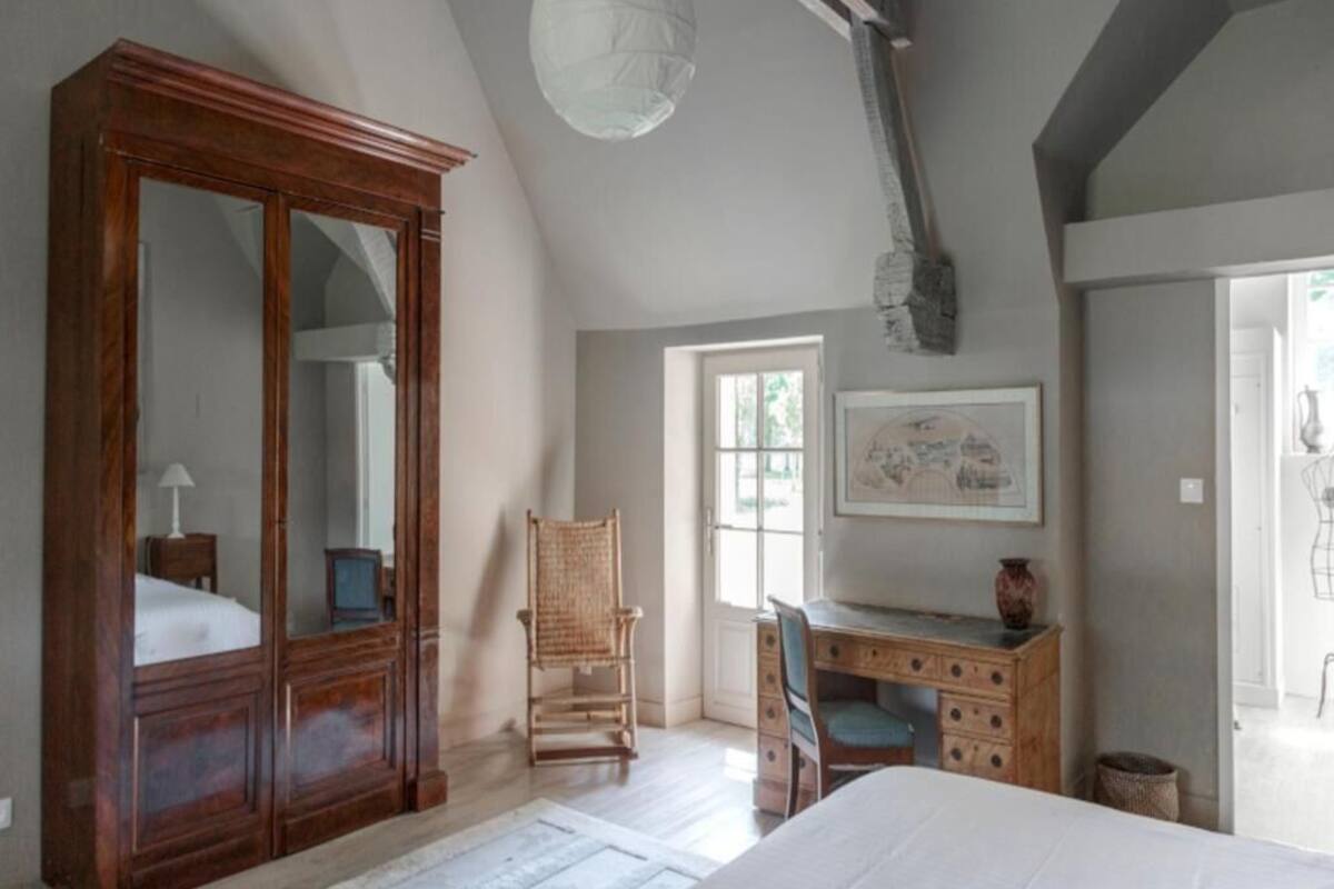 Une chambre dotée d’une grande armoire en bois, d’un bureau avec une chaise, d’un lit et d’une fenêtre laissant entrer la lumière naturelle.
