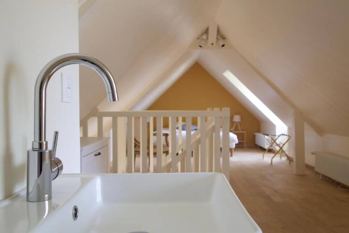 Une salle de bain moderne avec un lavabo blanc et un robinet chromé, un meuble-lavabo blanc et une rambarde blanche dans une pièce dont le plafond est en pente.