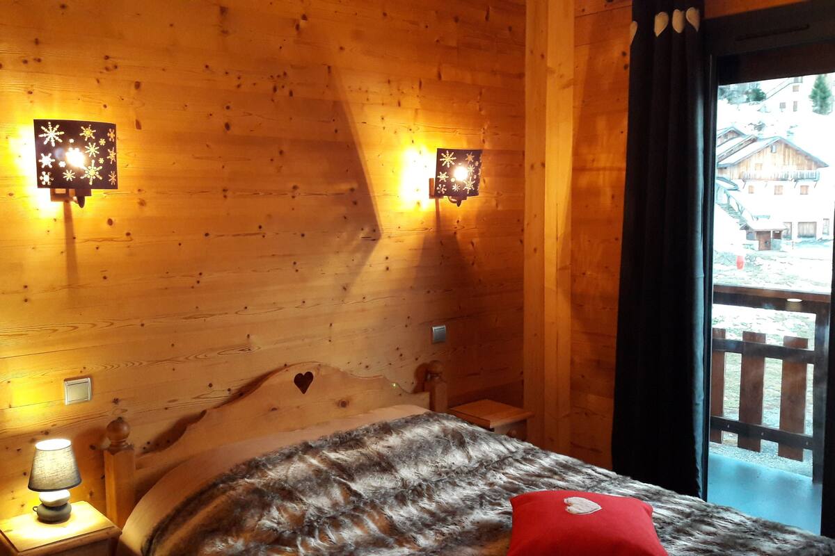 A wooden cabin room with a bed, a nightstand with a lamp, and two wall-mounted lights.