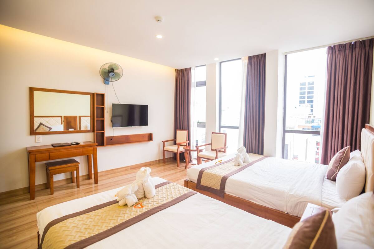 A hotel room with two beds, a desk, a chair, a TV, and a large window.