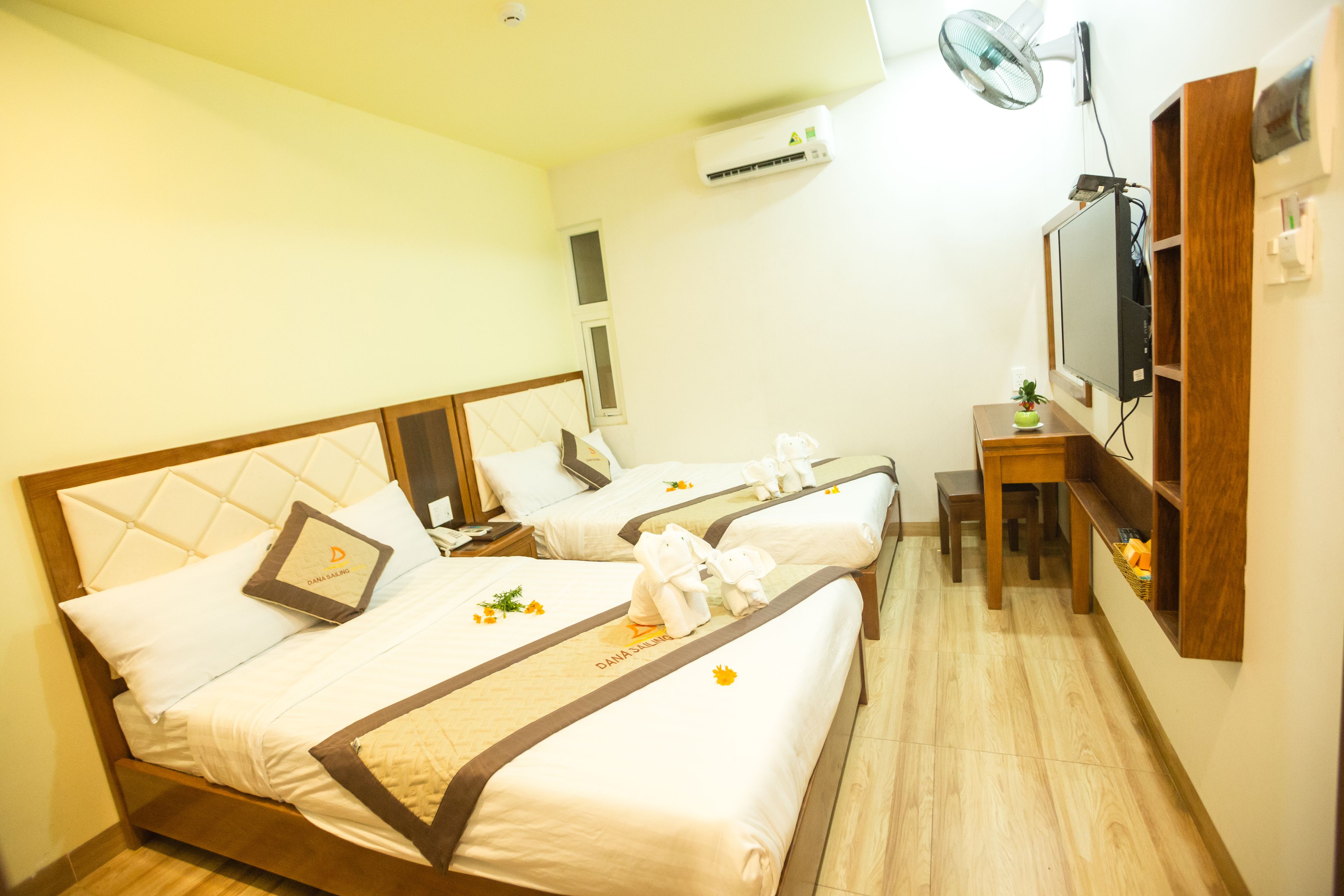 A hotel room with two beds, a desk, a chair, a TV, and an air conditioning unit.