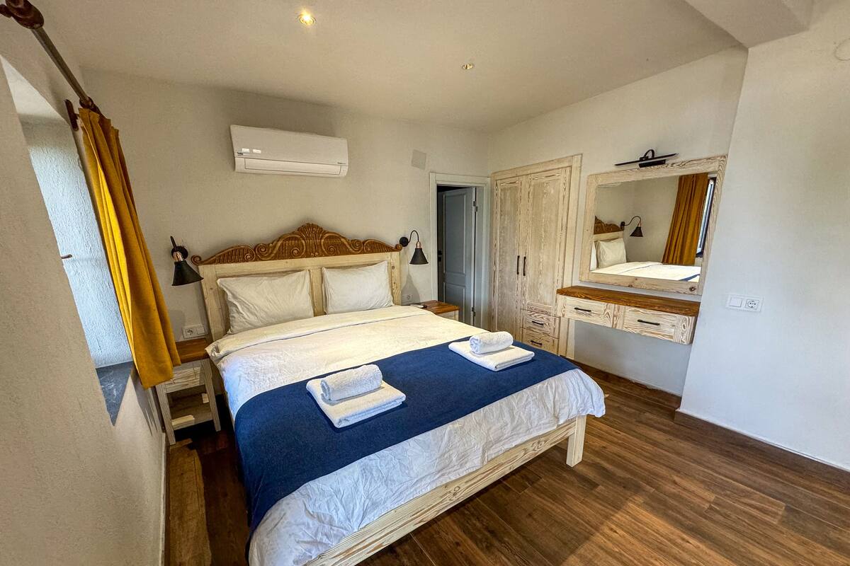 A bedroom with a wooden bed, a bedside table, a mirror, and a wardrobe.