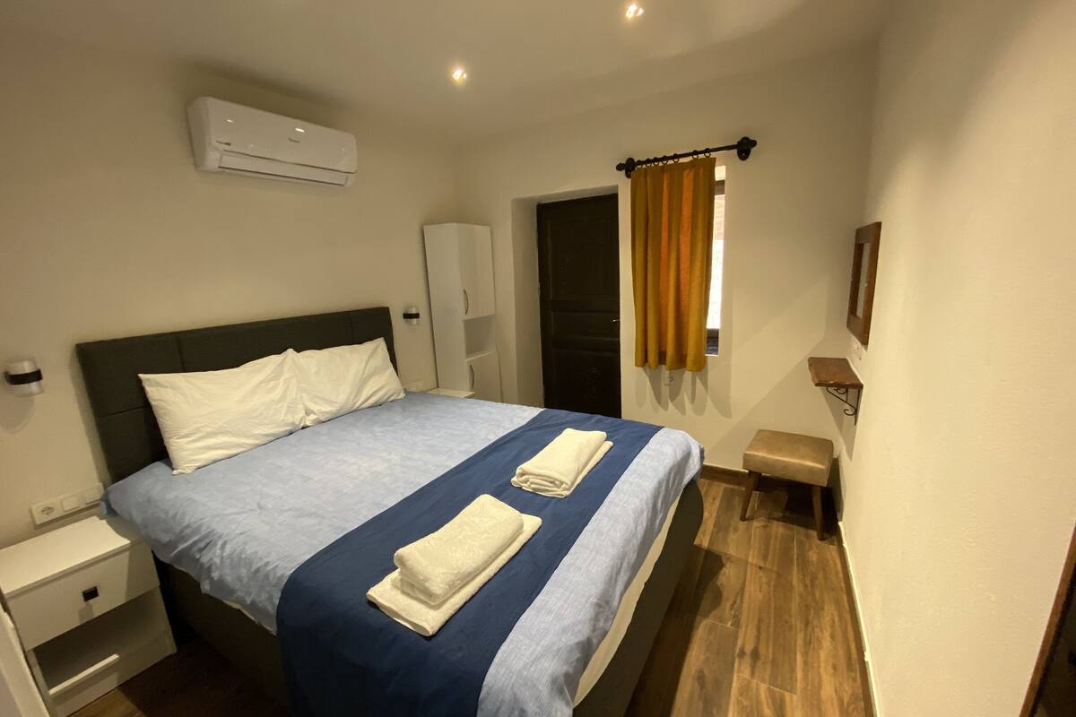 A hotel room with a bed, nightstand, wardrobe, and a window with curtains.