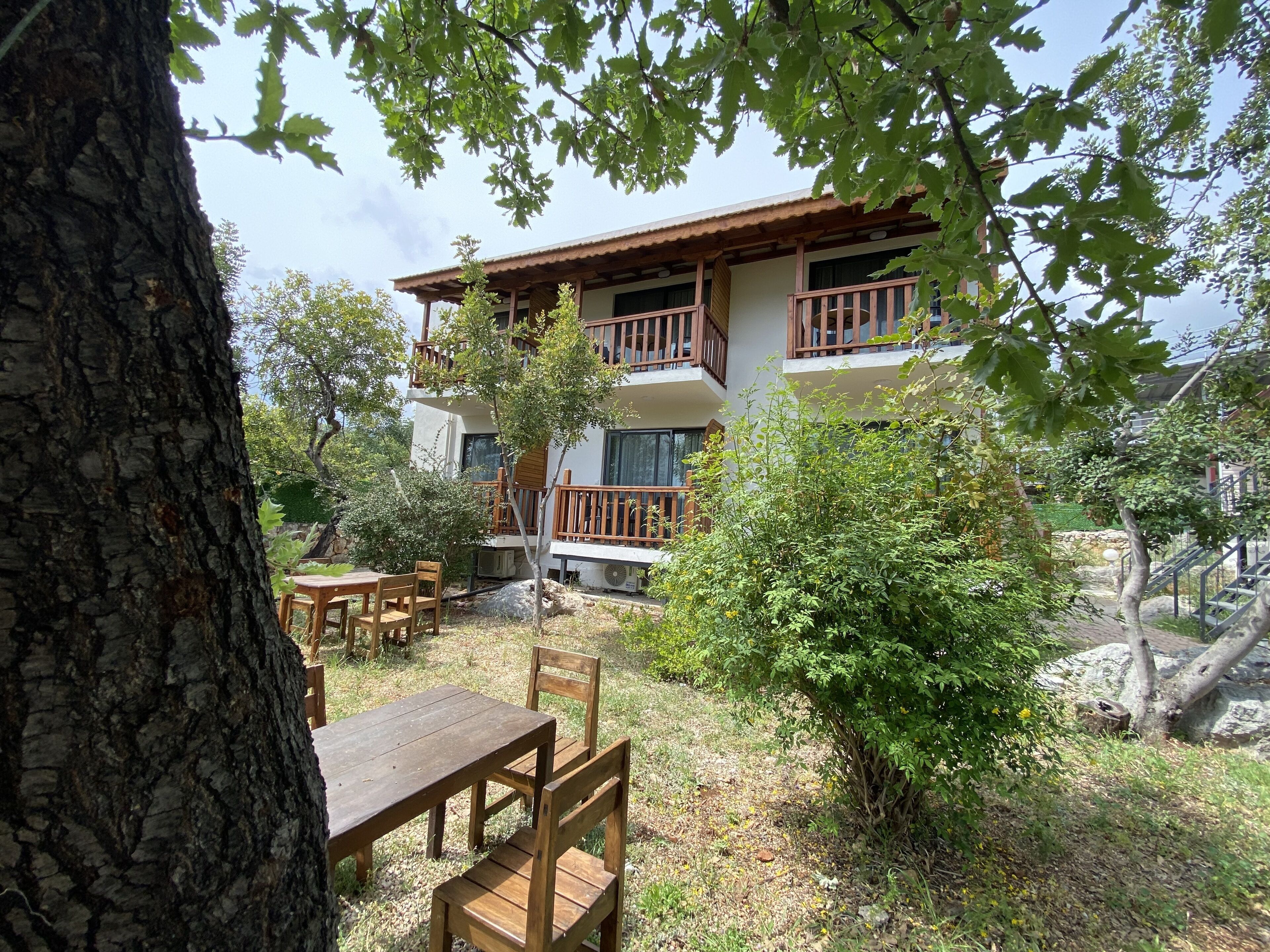 A two-story building with a balcony, surrounded by trees and a small patio area with a table and chairs.