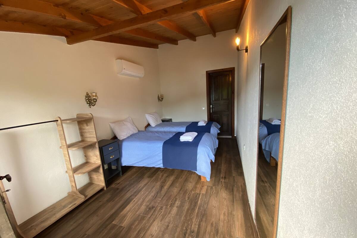 A bedroom with two beds, a wooden ladder, a nightstand, and a door leading to another room.