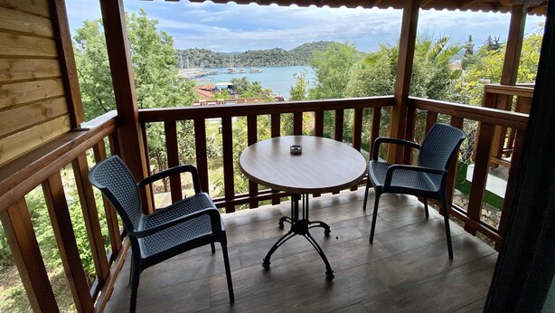A wooden deck with a table and two chairs, overlooking a scenic view of a lake and hills. - Ekin Pansiyon (Demre)
