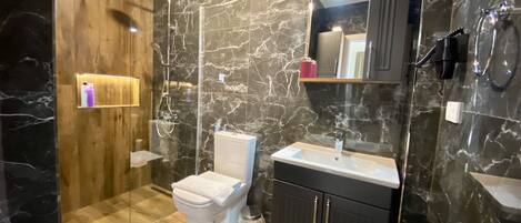 A modern bathroom with a marble wall, a wooden vanity, a white toilet, and a glass-enclosed shower.