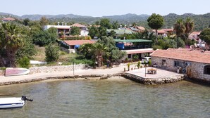 A coastal area with a stone pier, clear water, and buildings with red roofs. - Ekin Pansiyon (Demre)