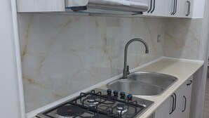 A compact kitchen with a gas stove, a sink, and white cabinetry. - White City Hostel (Baku)