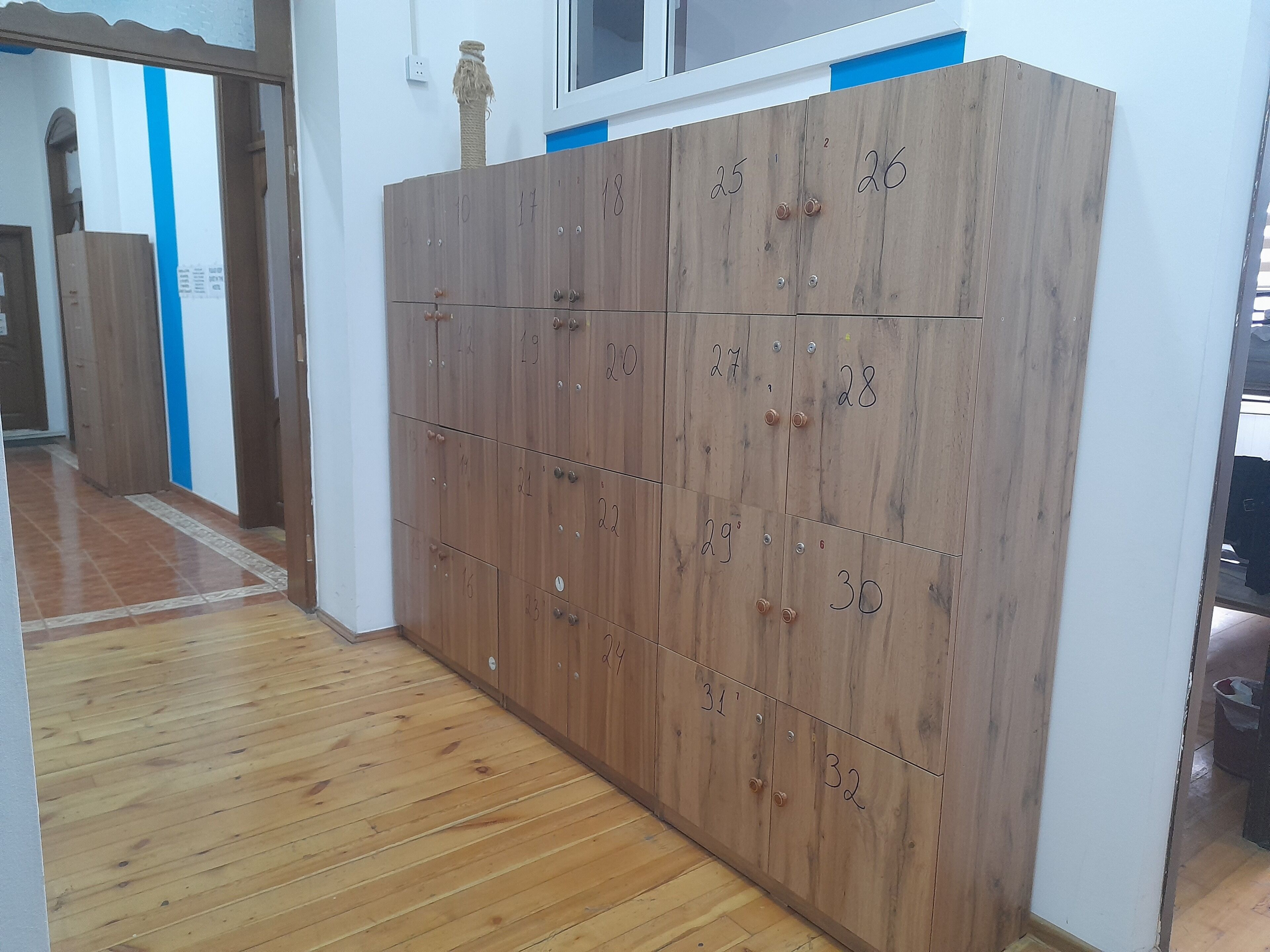 A hallway with wooden lockers numbered 1 to 32, a blue wall, and a window above the lockers.