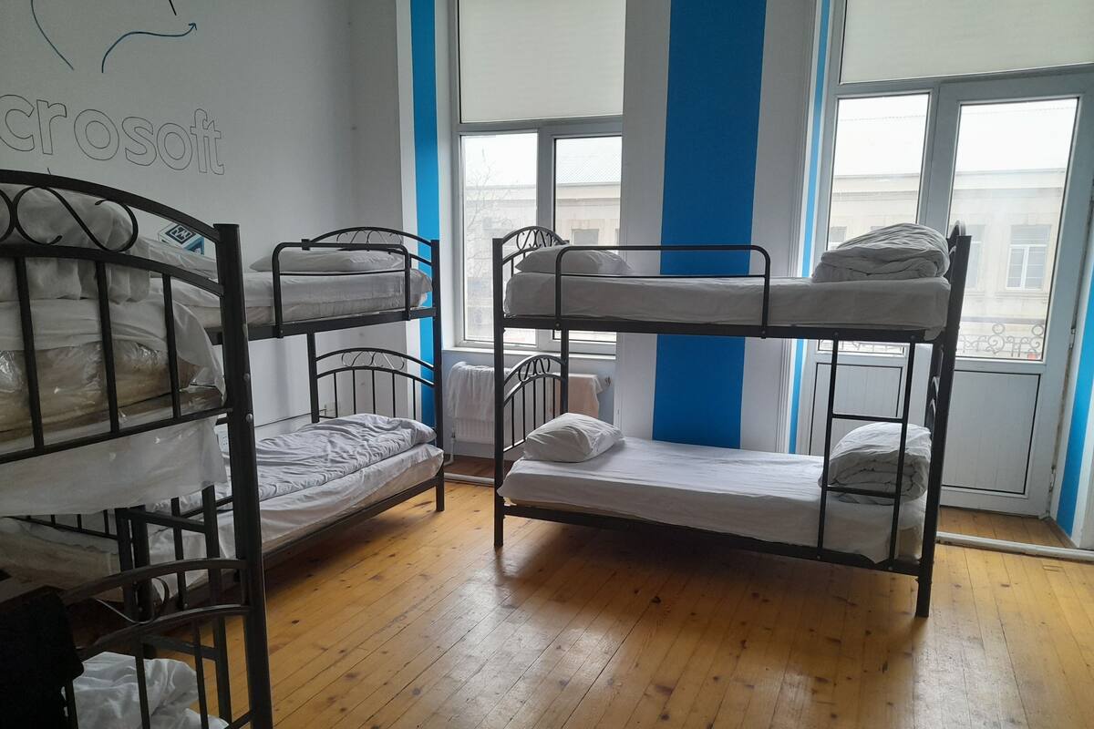 Un dormitorio con literas, suelo de madera, una ventana con vistas y una pared con un logotipo.