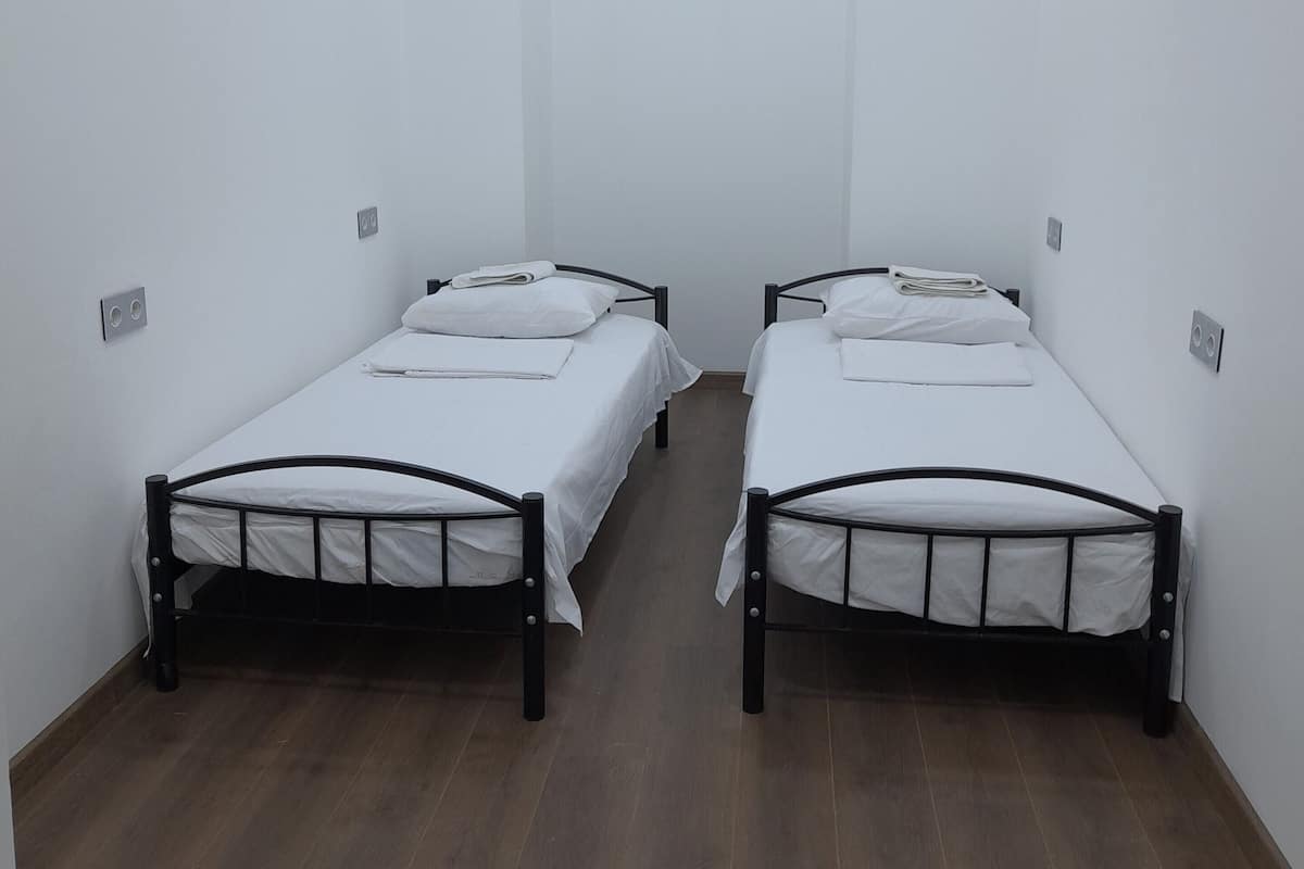 Una habitación con dos camas individuales, paredes blancas y suelo de madera.