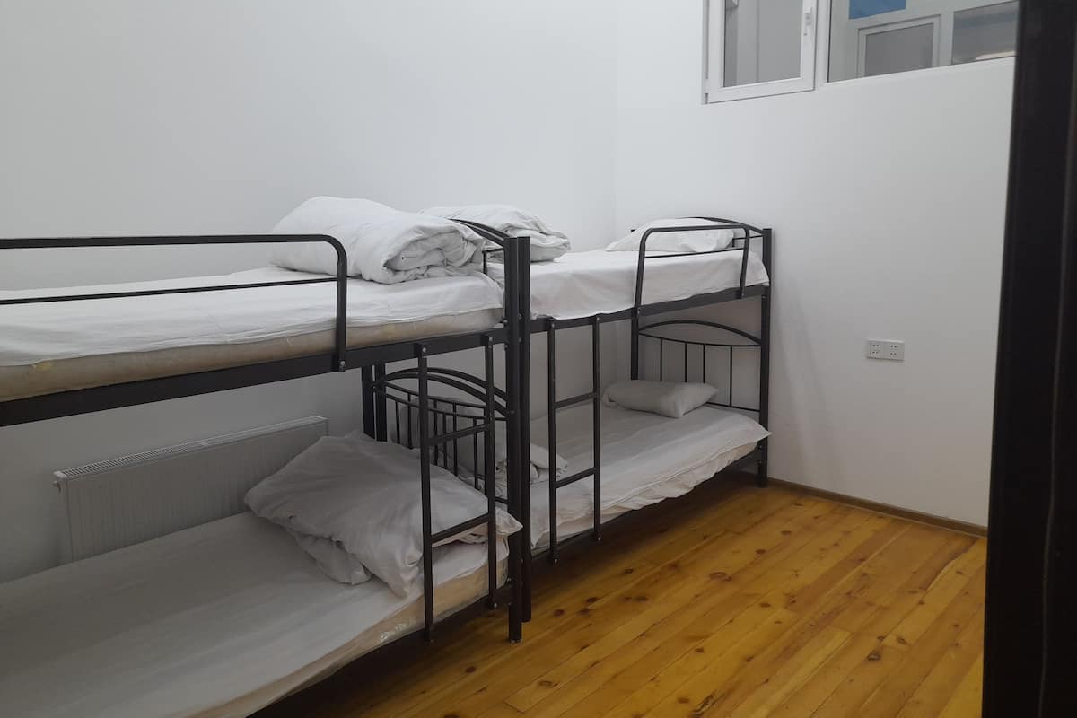 Habitación con literas, ropa de cama blanca y una ventana con cortina azul.