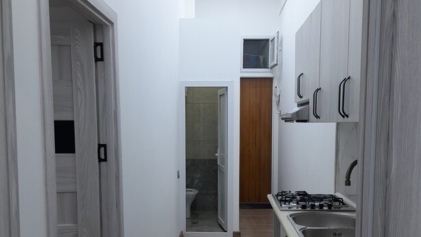A narrow hallway with a wooden floor, white walls, and a kitchen area with cabinets and a stove. - White City Hostel (Baku)