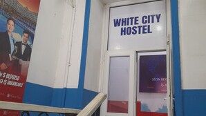 A hallway leading to the White City Hostel with a blue and white color scheme, a poster advertising job opportunities, and a security camera on the wall. - White City Hostel (Baku)