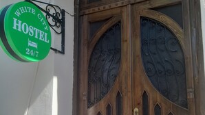 A wooden double door with decorative ironwork and a sign indicating a hostel with 24/7 availability. - White City Hostel (Baku)