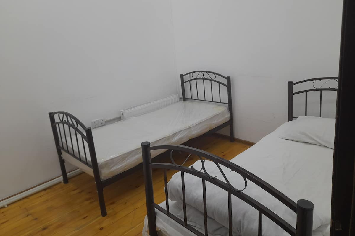 Habitación tipo dormitorio con dos camas individuales, suelo de madera, paredes blancas y un diseño sencillo y funcional.