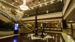 A spacious lobby with a grand chandelier, a staircase, and a reception desk.