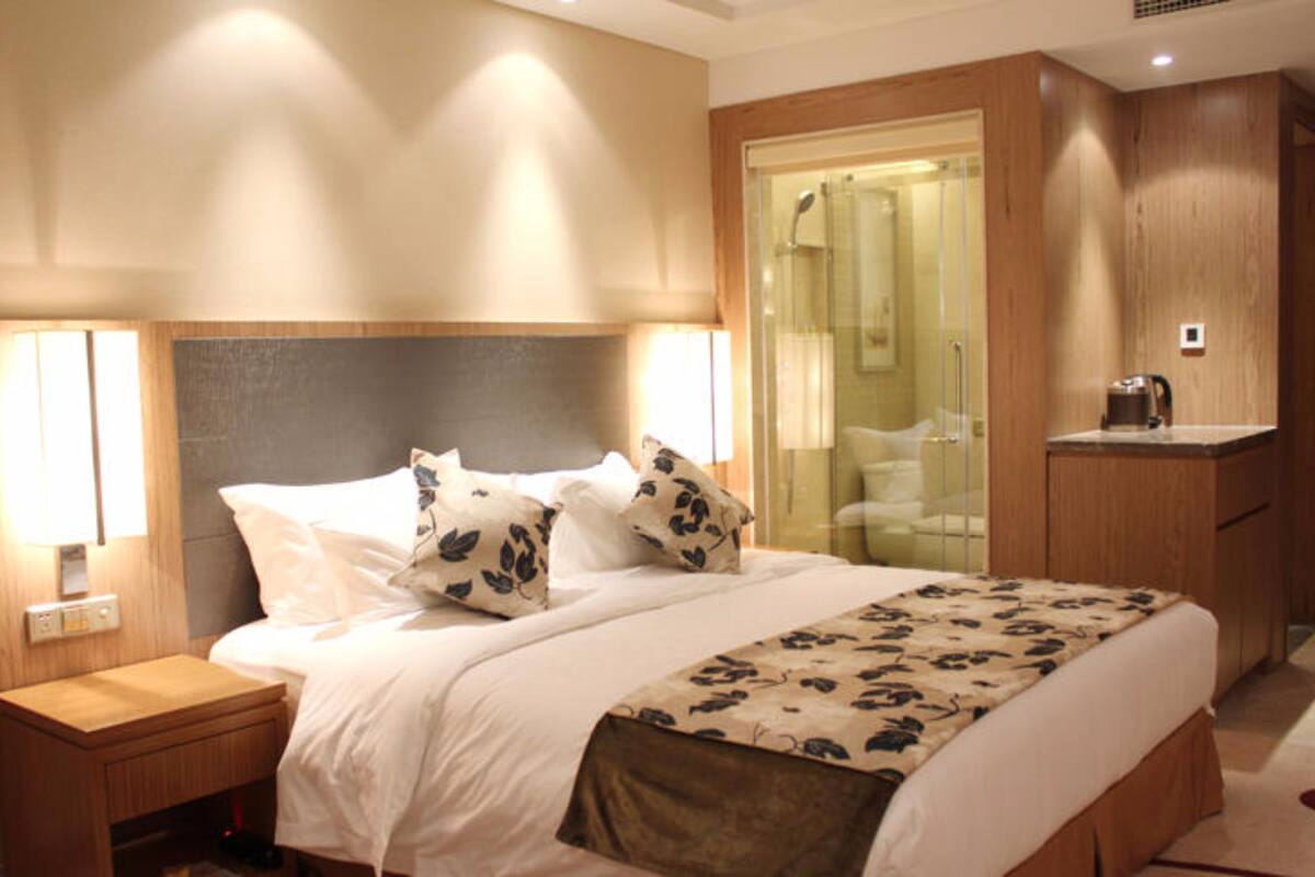 Une chambre d’hôtel avec un grand lit, une table de chevet, une armoire en bois et une cabine de douche en verre.