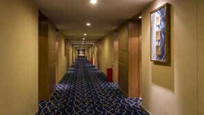 A hotel hallway with patterned carpet, wooden doors, and a framed artwork on the wall.