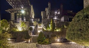 A stone building with a staircase leading to a second floor, surrounded by greenery and illuminated by artificial lighting. - Ostra Menalon Luxury Suites (Tripoli)