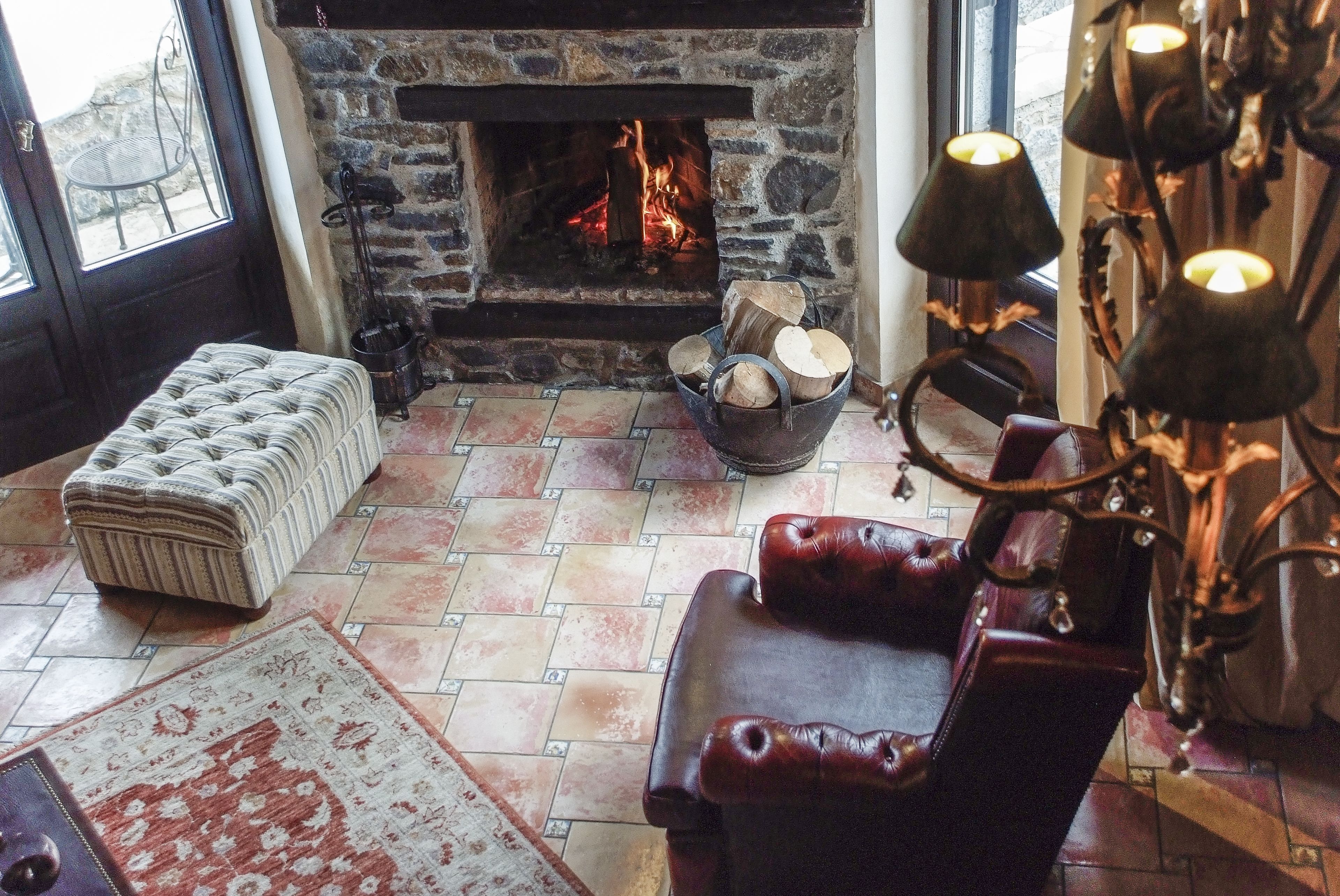Una sala de estar acogedora con chimenea de piedra, un sillón de cuero, un otoman acolchado y una lámpara decorativa.