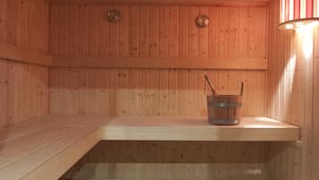 Uma sauna com paredes e bancos de madeira, um balde com uma escova e uma luminária fixada na parede.