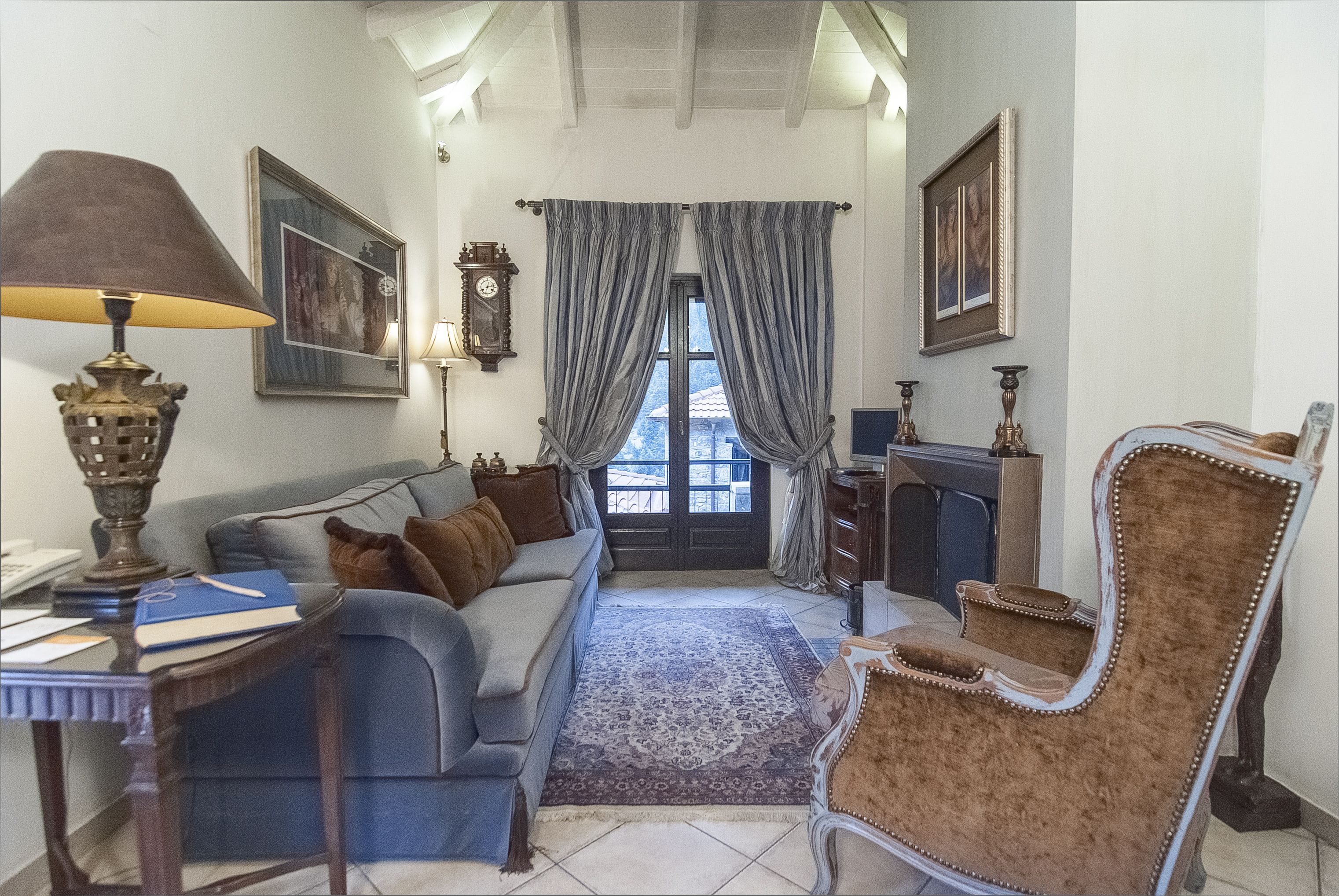 Una sala de estar con un sofá, una silla, una mesa con lámpara y una alfombra. Hay cortinas en la ventana y un reloj en la pared.