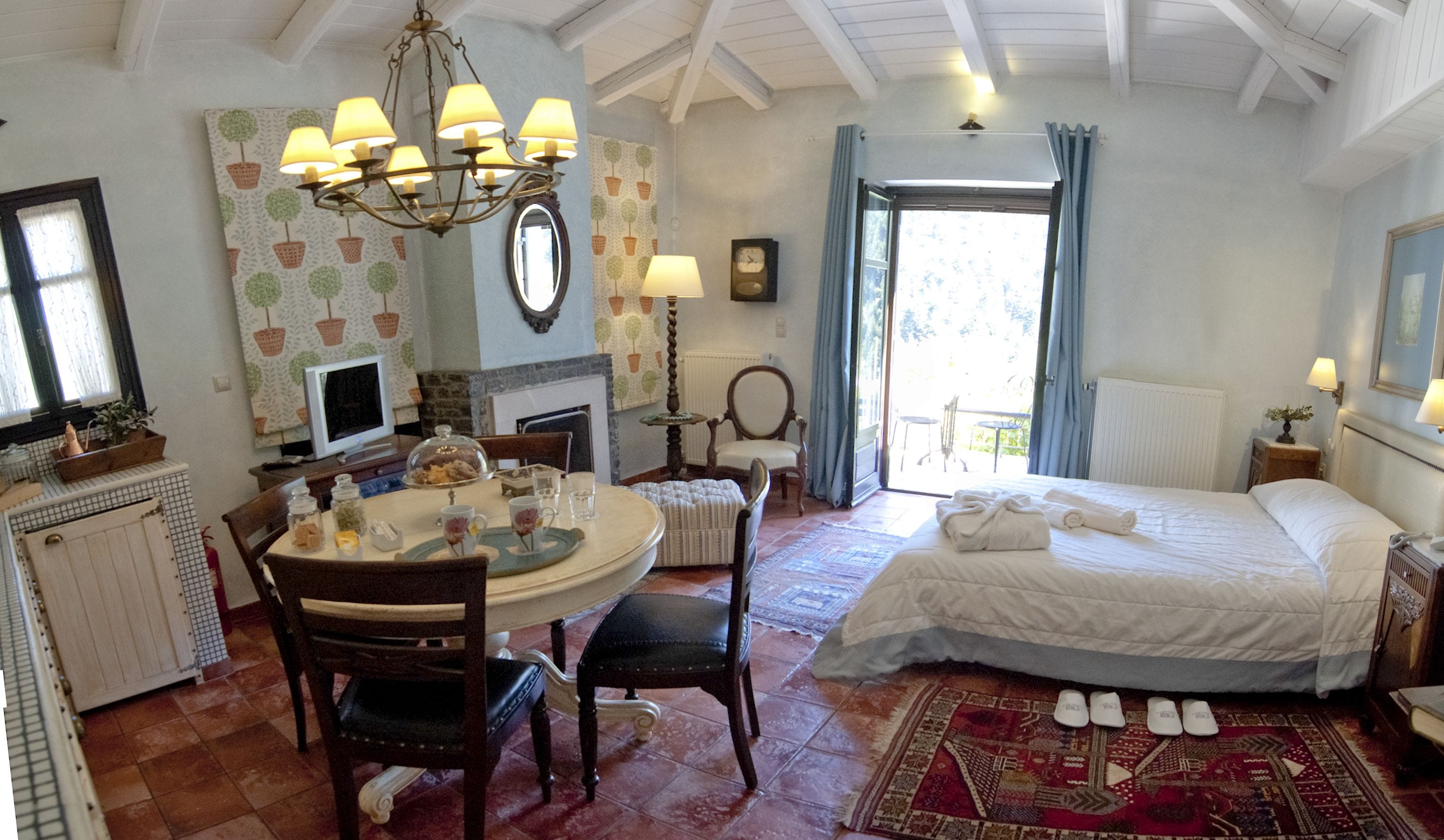 Una habitación acogedora con cama, una mesa de comedor con sillas, una araña, una chimenea y vistas al exterior.