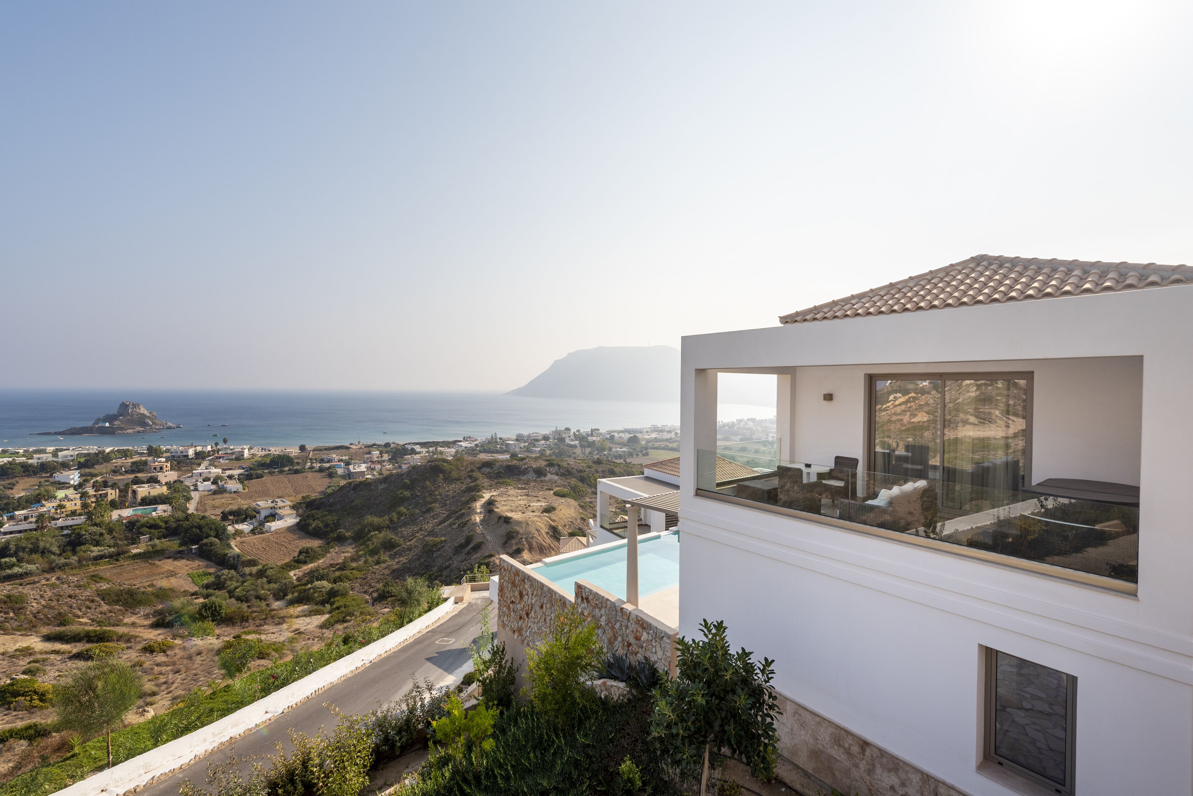 A modern villa with a large glass balcony overlooking a coastal landscape.