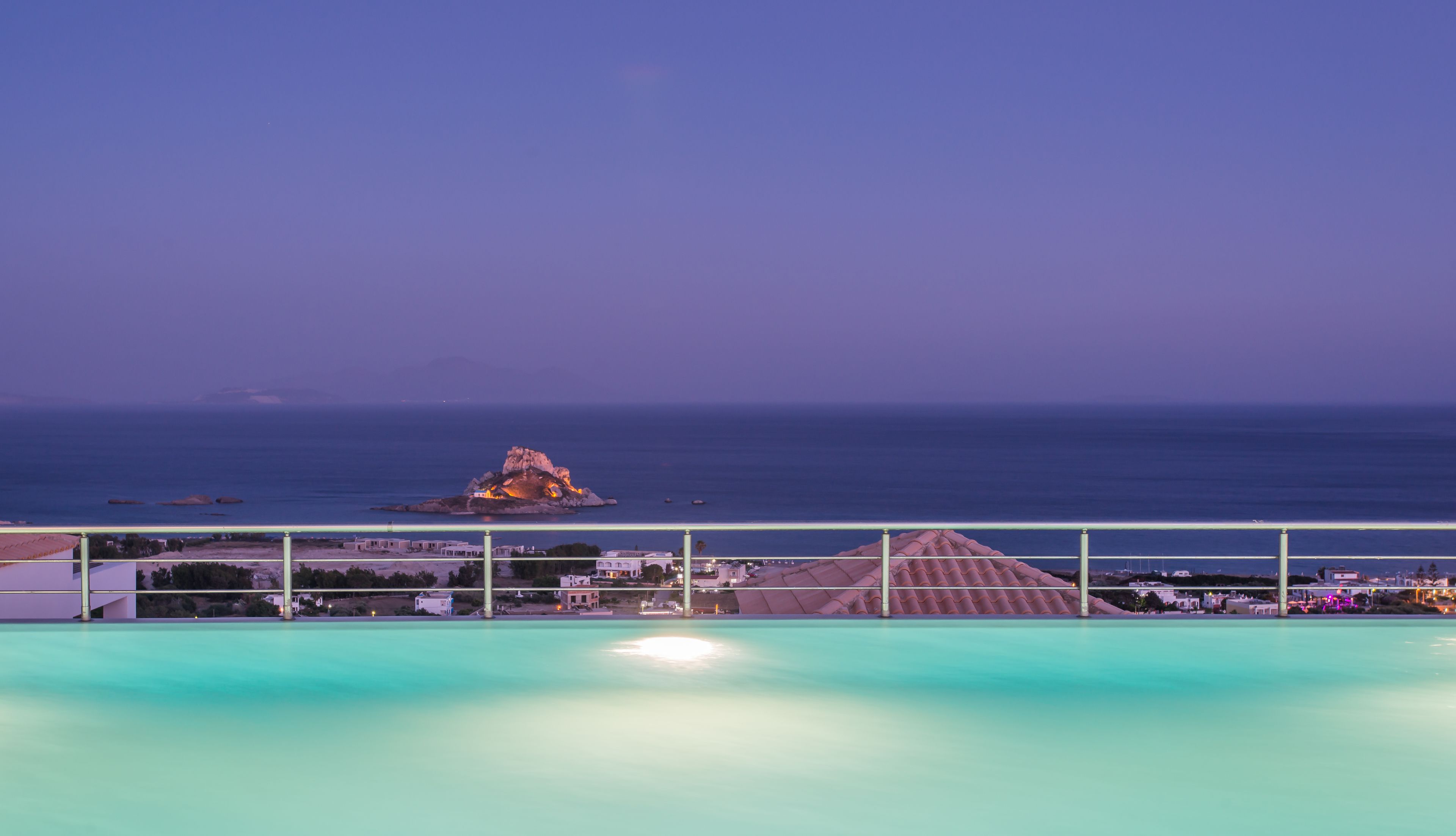 A pool with a view of the sea and a rocky island in the distance.