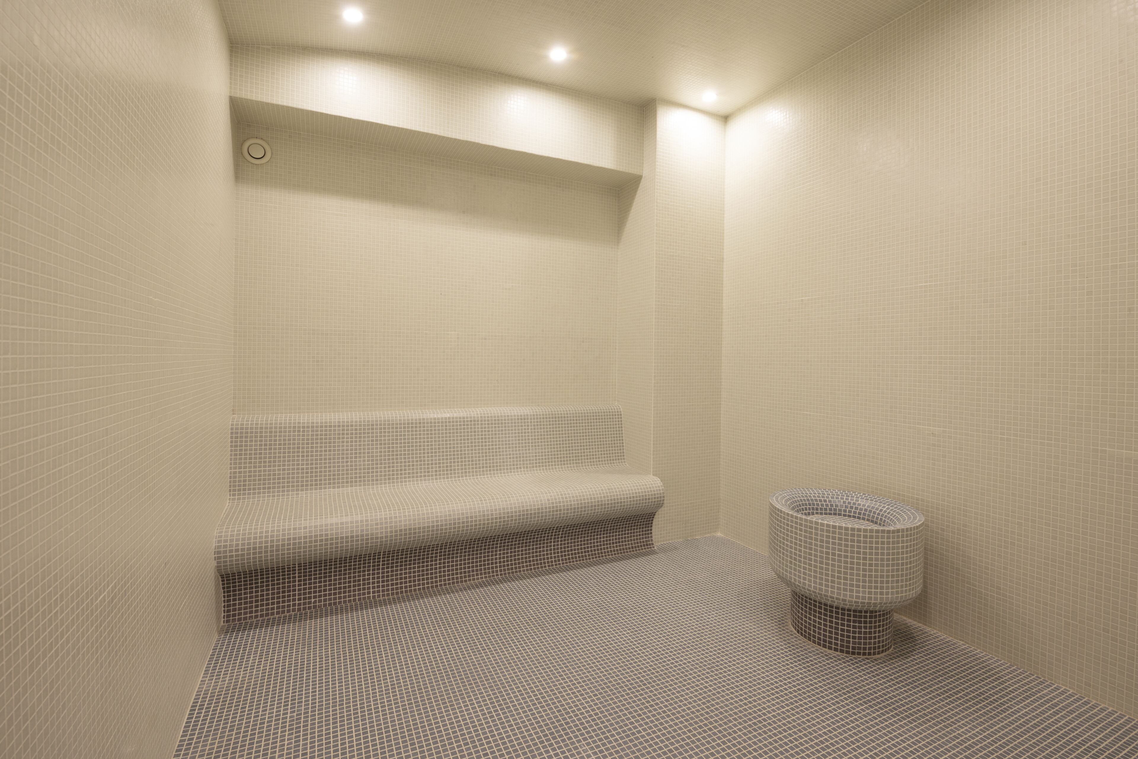 A modern bathroom with a tiled floor and walls, a built-in bench, and a round, textured sink.