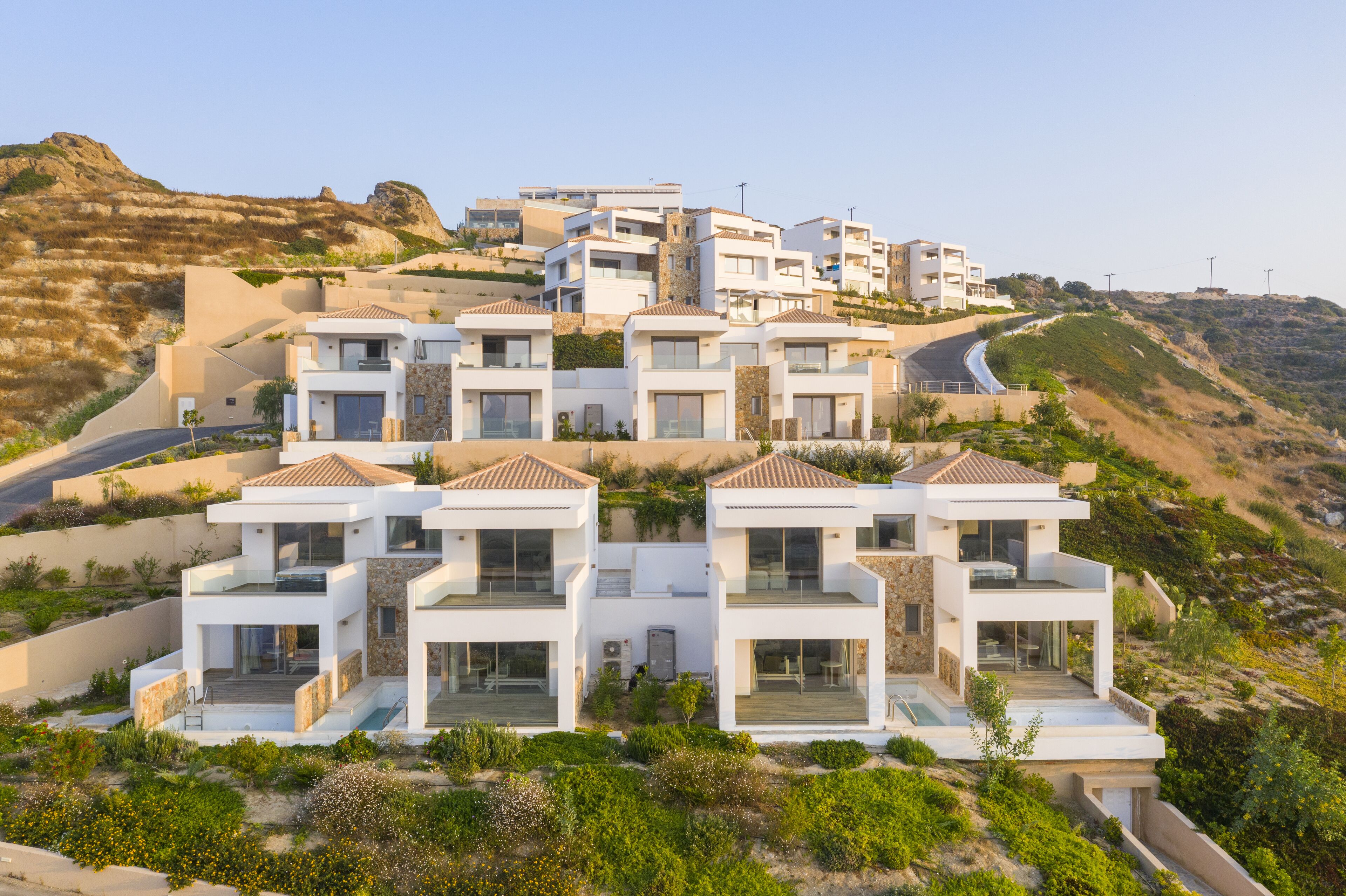 Un moderno complejo residencial con varias edificaciones de dos pisos, con balcones y ventanas amplias, ubicado en una ladera con vista despejada del paisaje circundante.