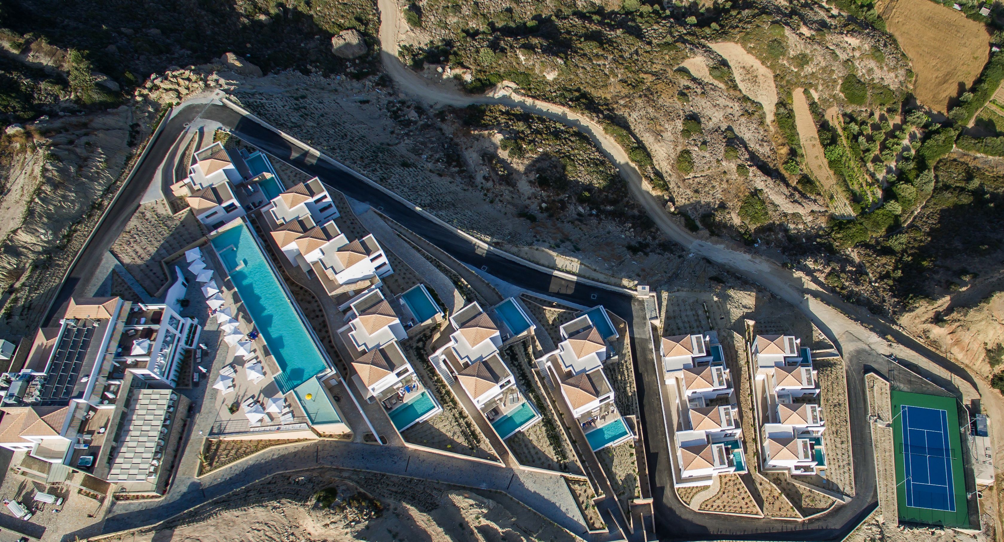 An aerial view of a resort with multiple swimming pools, a tennis court, and a winding road.