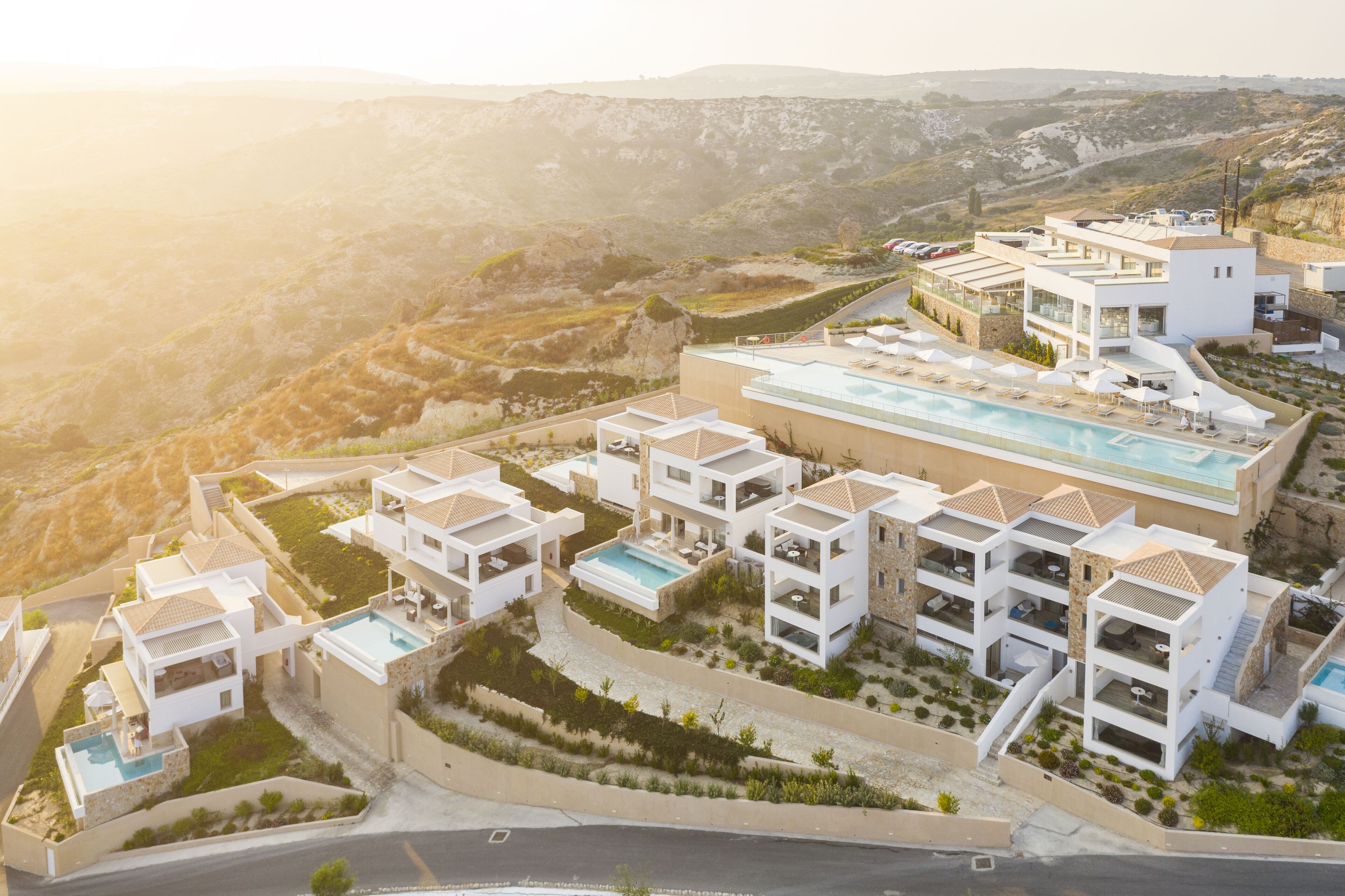 A modern resort with multiple buildings, swimming pools, and a scenic hillside backdrop.