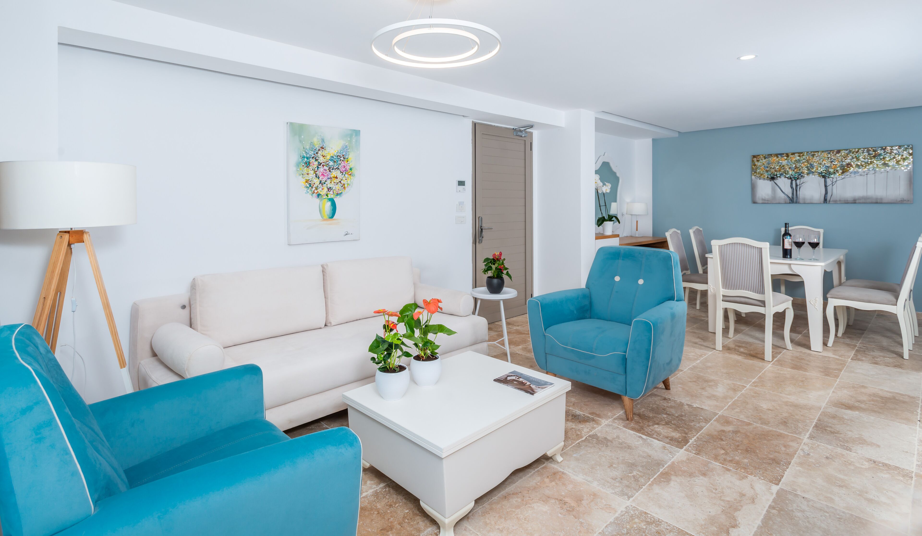 A modern living room with a sofa, two armchairs, a coffee table with plants, and a dining area with chairs and a table.