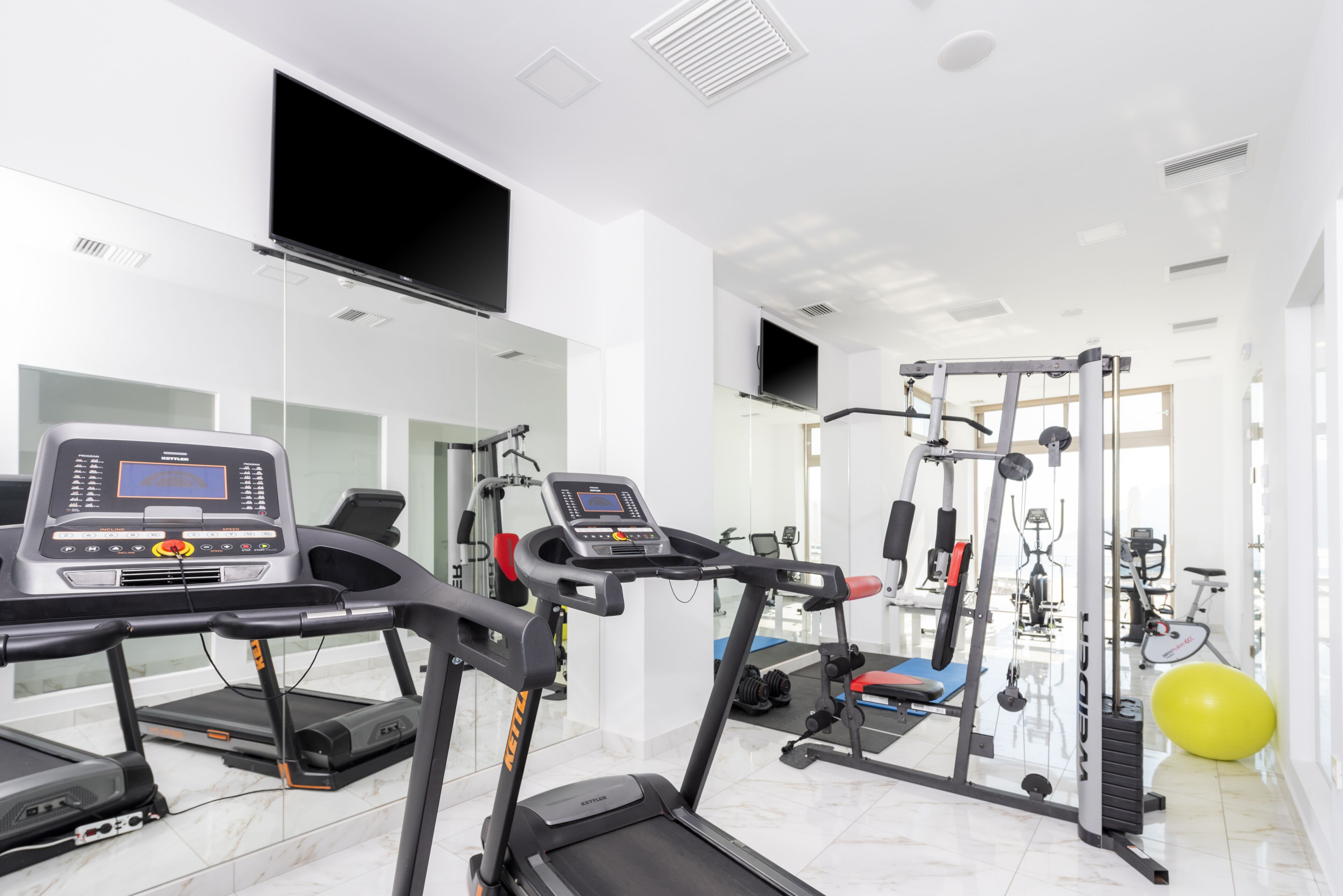 Une salle de sport moderne équipée de tapis de course, d’appareils de musculation et d’un grand ballon d’exercice.