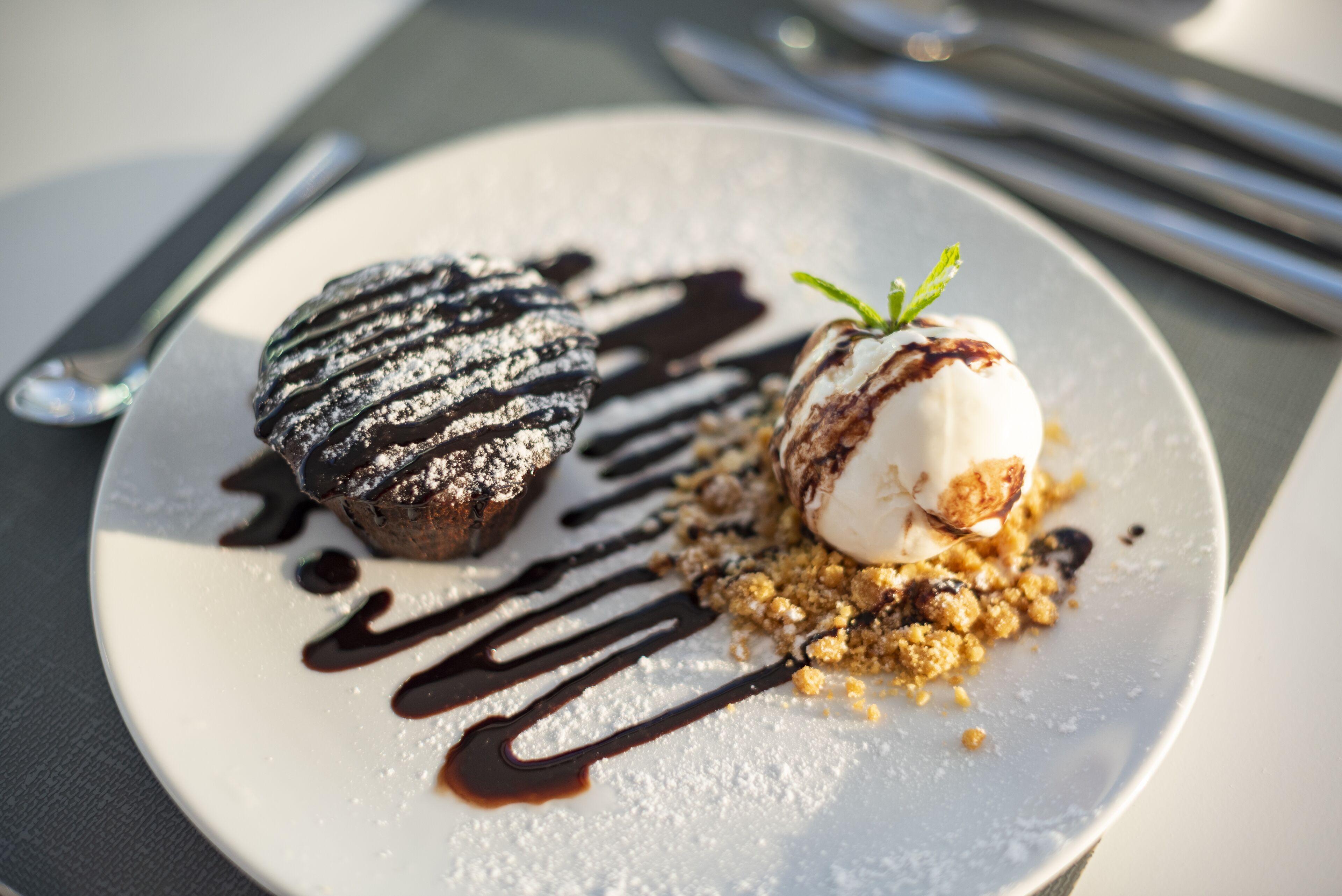 Une assiette à dessert avec une tarte au chocolat et une boule de glace à la vanille, le tout nappé de sauce au chocolat, sur une assiette blanche.