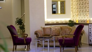 A living room with a sofa, two armchairs, a glass coffee table, a mirror, and a patterned wall. - Aygoren Otel Denizli (Denizli)