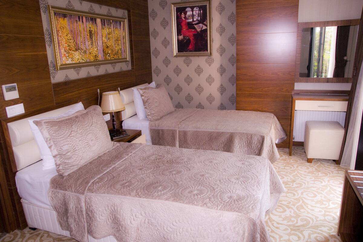 A hotel room with two beds, a desk, a chair, and a mirror.
