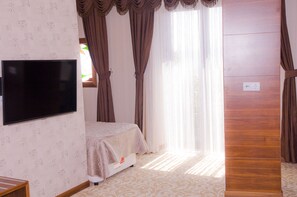 Una habitación con una cama, un televisor de pantalla plana montado en la pared y un amplio ventanal con cortinas.