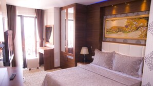 Una habitación de hotel con cama, escritorio, silla, televisor y un cuadro en la pared.