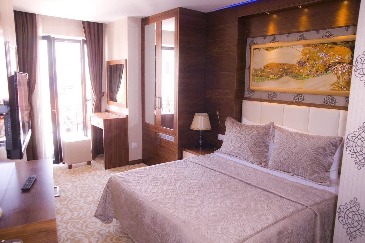 A hotel room with a bed, a desk, a chair, a TV, and a painting on the wall.