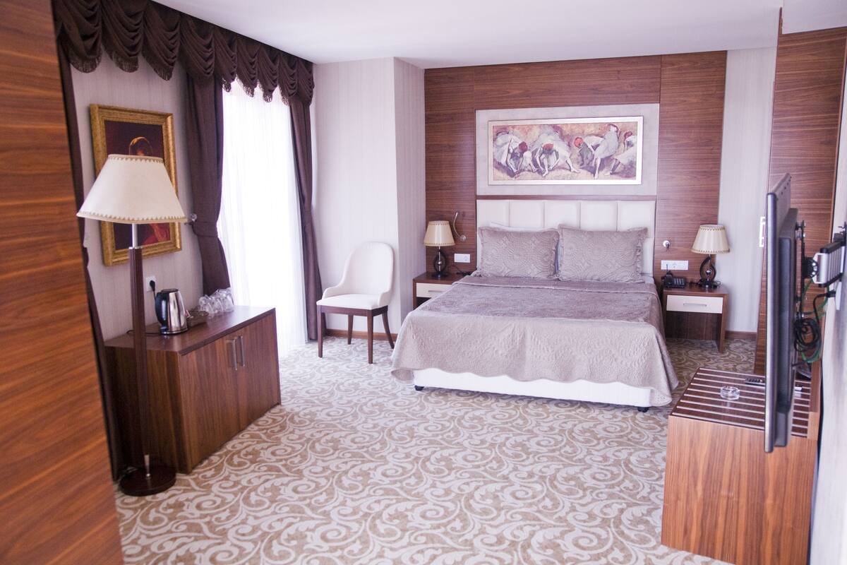 A hotel room with a large bed, two bedside tables with lamps, a chair, a wooden cabinet, and a framed picture on the wall.