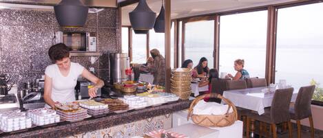 Montaje de bufé con diferentes alimentos y vista al mar a través de amplios ventanales.